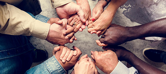 A table with a group of people holding hands praying. Prayer is a vital part of Christian life. LivePrayer.r